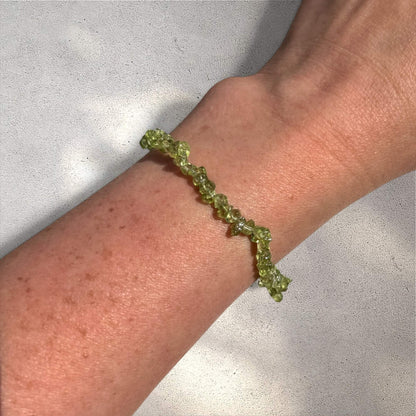 A bright green peridot crystal chip bracelet on a wrist against a neutral background