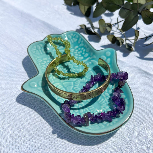 A turquoise hamsa hand trinket dish with crystal chip bracelets and a brass intention bracelet sold in the UK