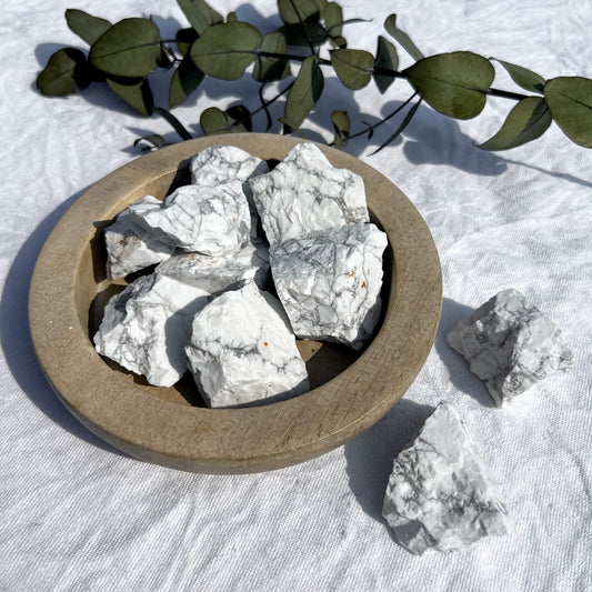 A wooden dish overflowing with white and grey marbled Howlite raw crystal pieces