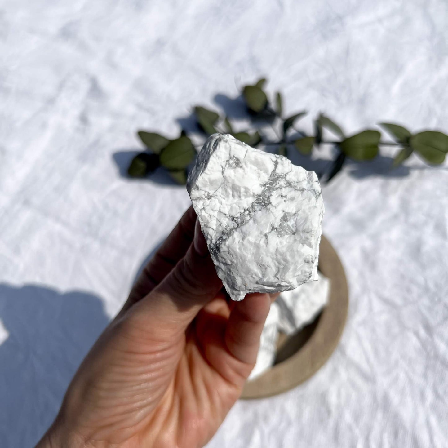 A white and grey marbled howlite crystal piece is held to camera to show a silvery streak running through the crystal