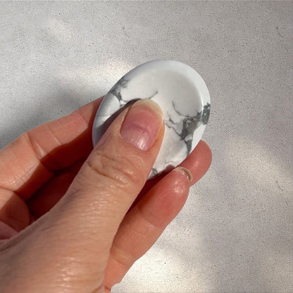 Rock + Realm Crystals white and grey marbled Howlite crystal worry stone with thumb indentation held in-between thumb and forefinger