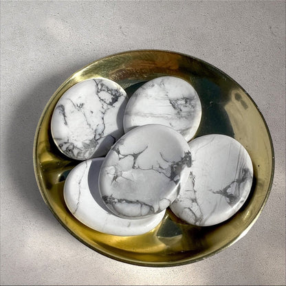 Rock + Realm Crystals polished white and grey marbled Howlite oval worry stones with thumb indentation shown in a brass dish from above