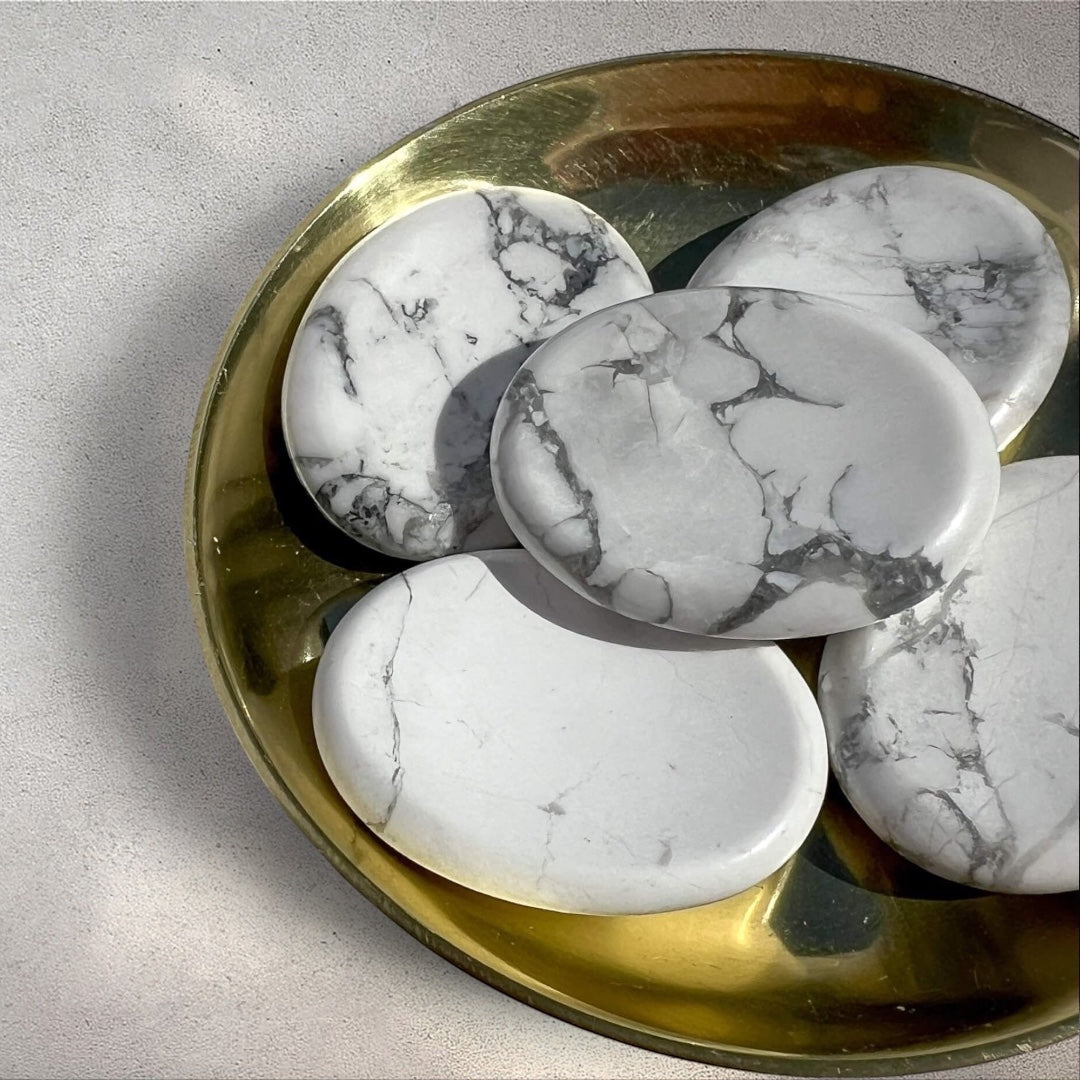 Rock + Realm Crystals white and grey marbled Howlite oval worry stones with thumb indentation in a brass dish