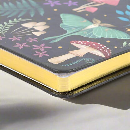 Rock + Realm Crystals Dark Forest A5 journal with a luna moth, mushrooms, and floral illustrations on a dark background. Features gold-gilded page edges.
