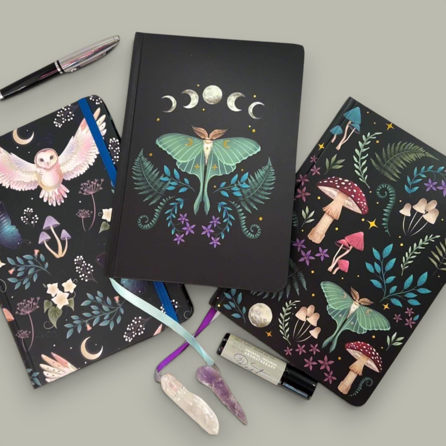 Rock + Realm Crystals black journals with mystical designs: owl, luna moth, mushrooms, ferns, and moon phases. Includes crystals and pen.