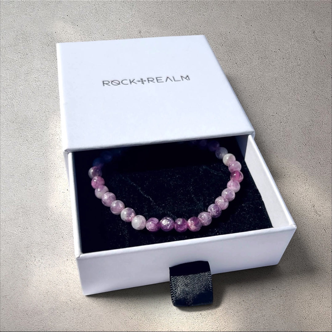 Pink and lilac Lepidolite crystal bead bracelet in a 'Rock + Realm' box on a white fabric background