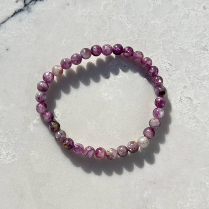 Pink and lilac Lepidolite crystal bead bracelet on a white and grey marble surface