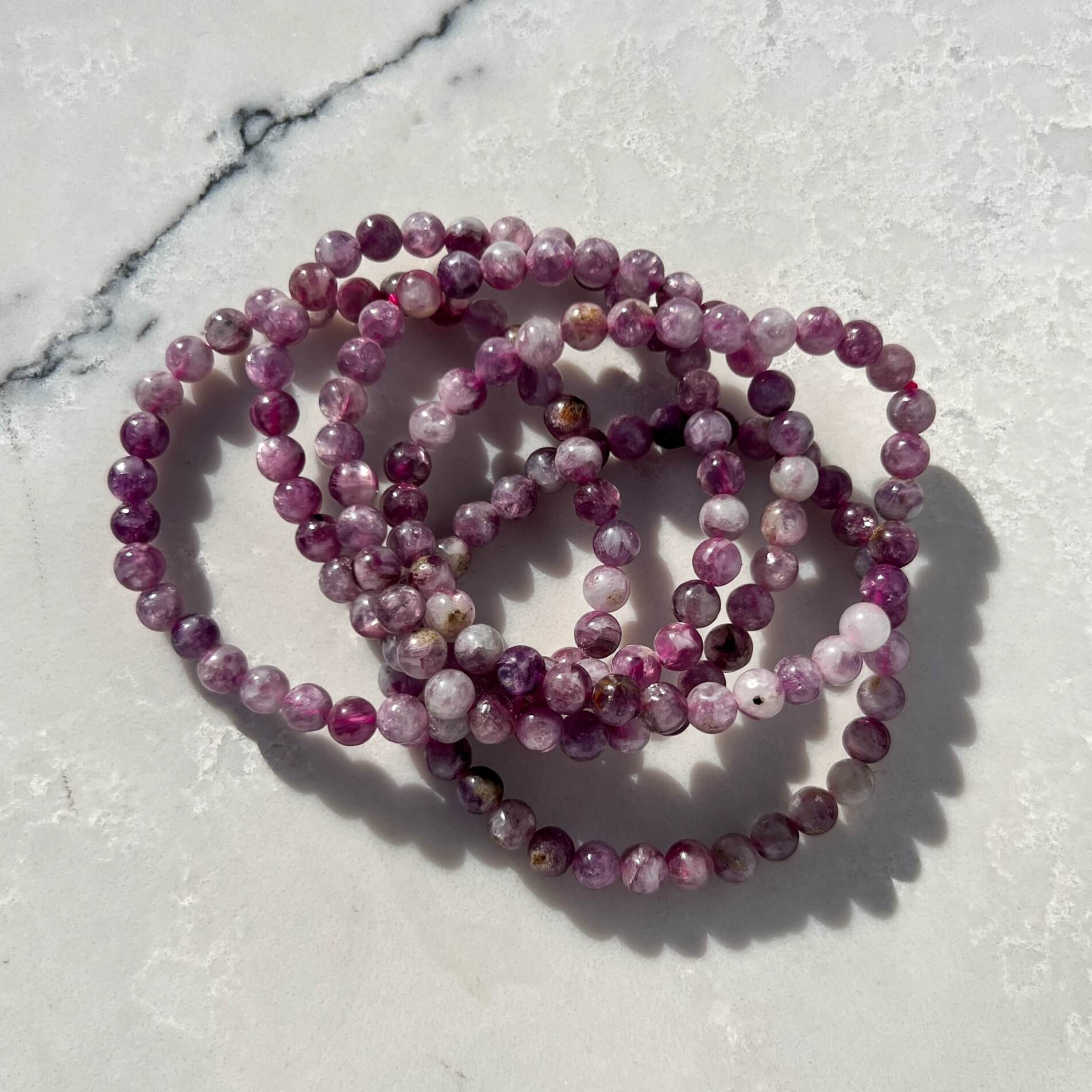 Stack of four pink and lilac Lepidolite crystal bead bracelets on a marble textured surface