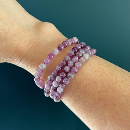 Stack of 4 Pink and lilac Lepidolite crystal bead bracelets on a woman's wrist against a teal background
