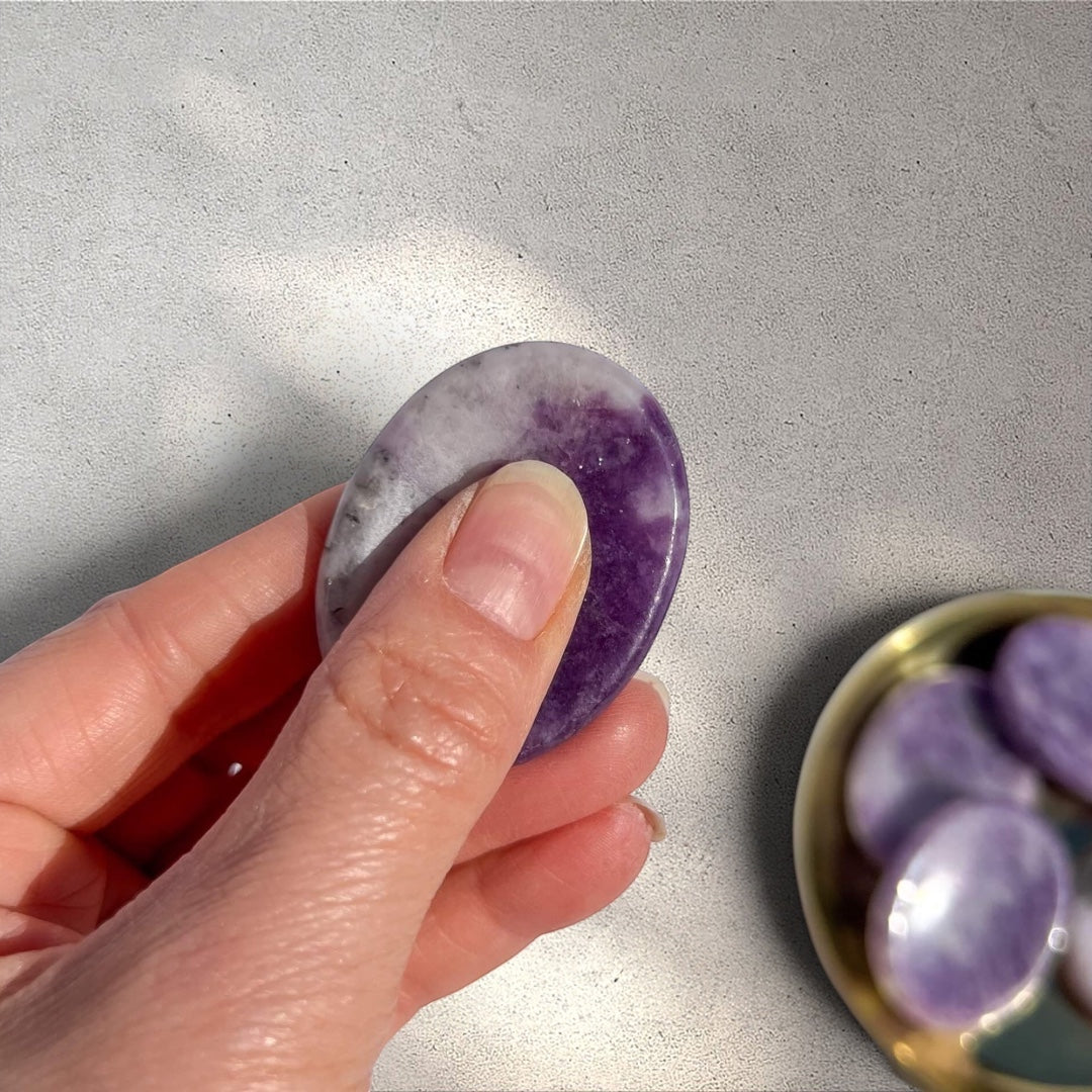 Rock + Realm Crystals Lepidolite worry stone with purple and white marbling, held between thumb and forefinger