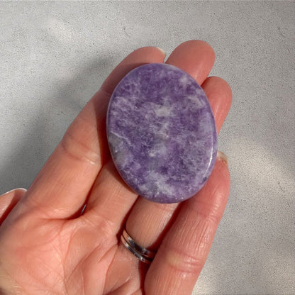 Rock + Realm Crystals Lepidolite worry stone, oval-shaped, smooth purple with white mica inclusions, held in a hand.