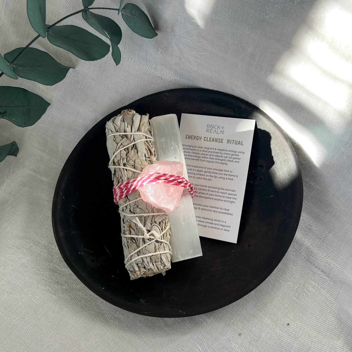 Aerial shot of Sage, selenite and rose quartz bundle on a black dish with an energy cleanse ritual card