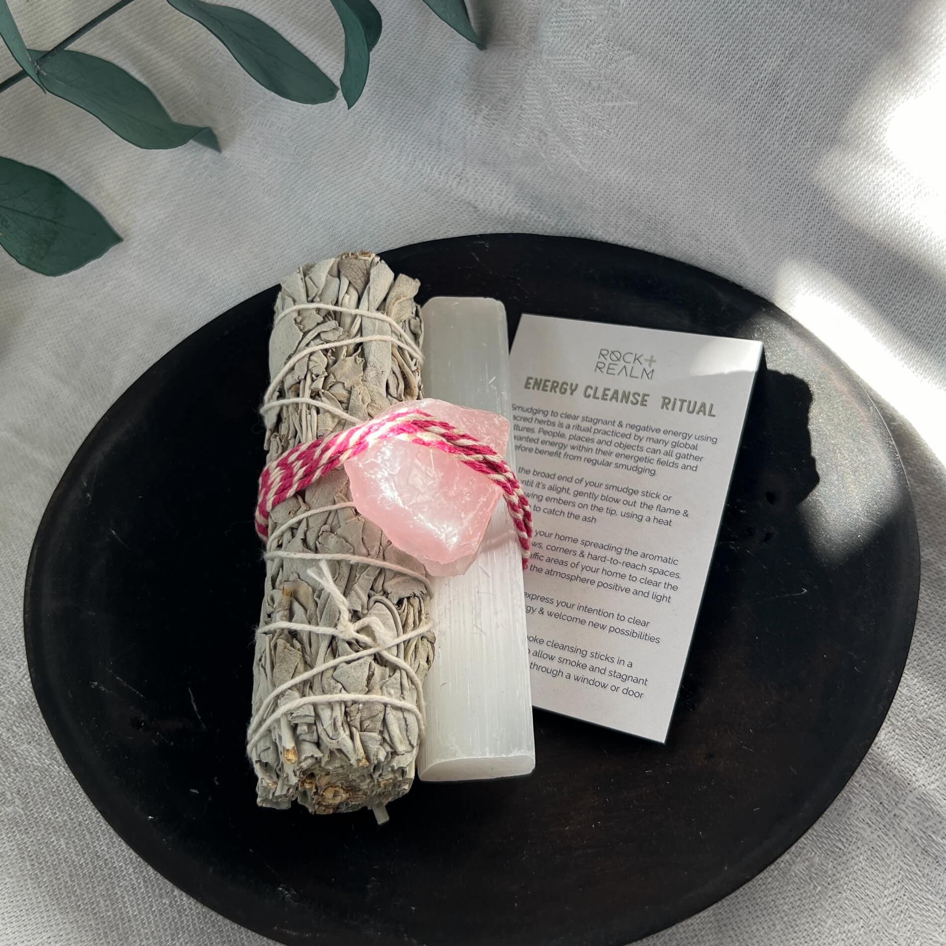 Sage, selenite and rose quartz bundle on a black dish with an energy cleanse ritual card close up