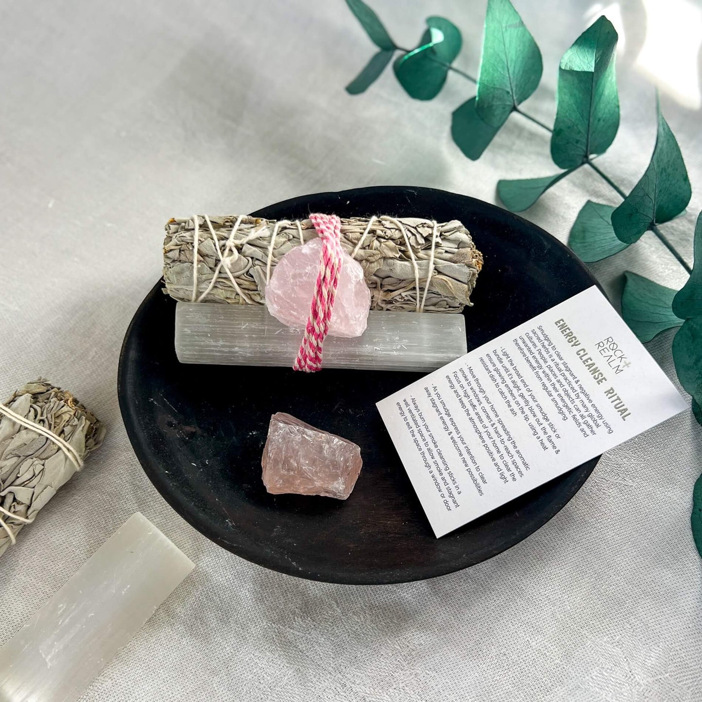 Sage, selenite and rose quartz bundle on a black dish with an energy cleanse ritual card