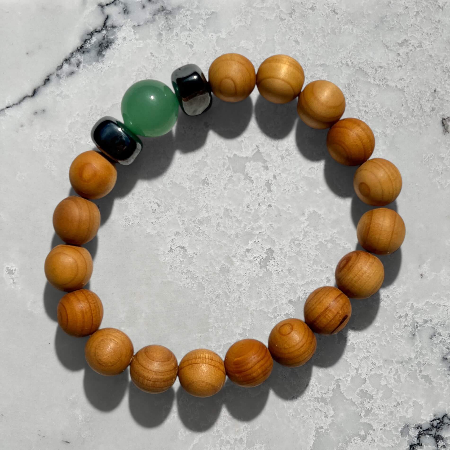 Cedar wood beaded bracelet with green aventurine and metallic black hematite beads on a marble surface