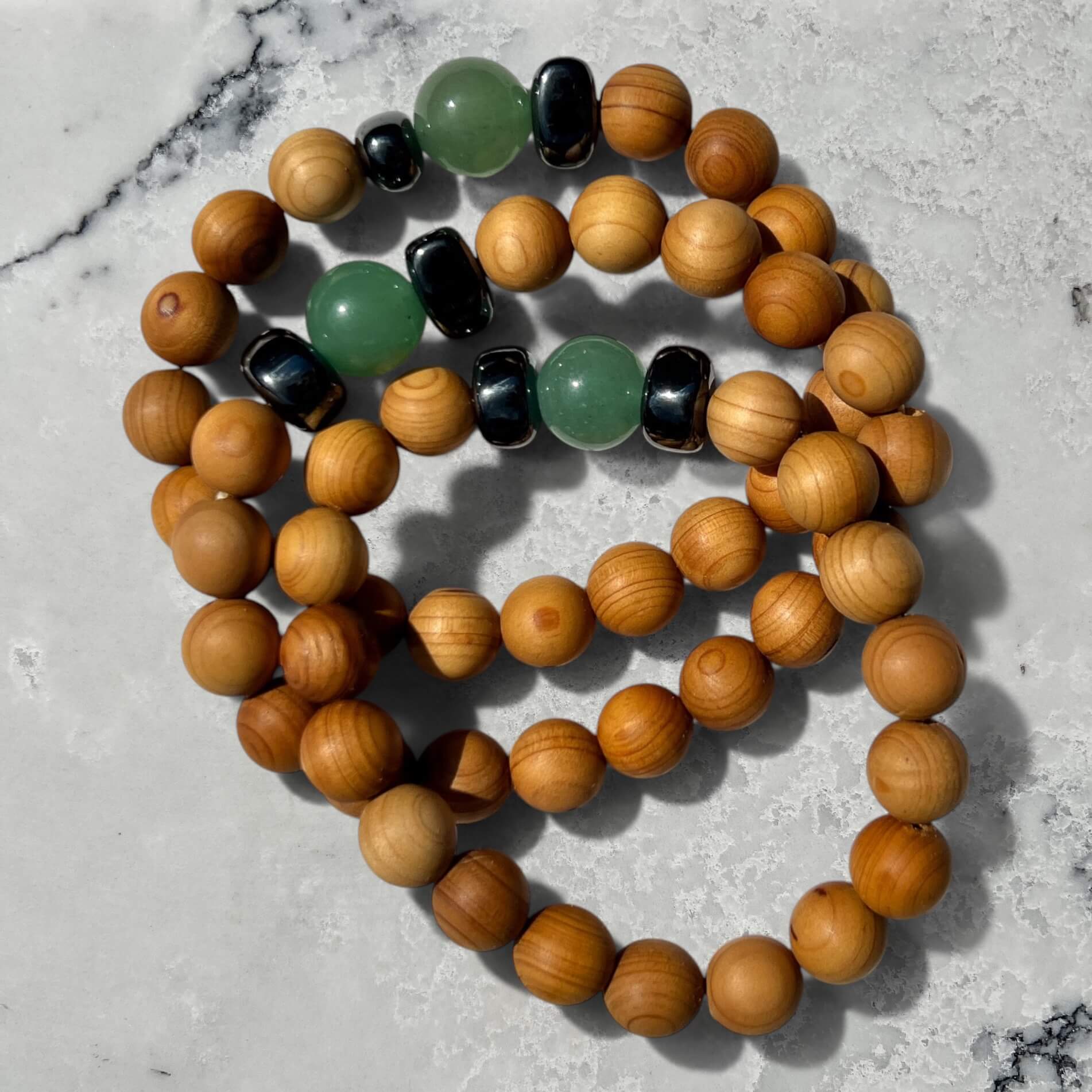 Stack of 3 Cedar wood beaded bracelets with green aventurine and metallic black hematite beads on a marble surface