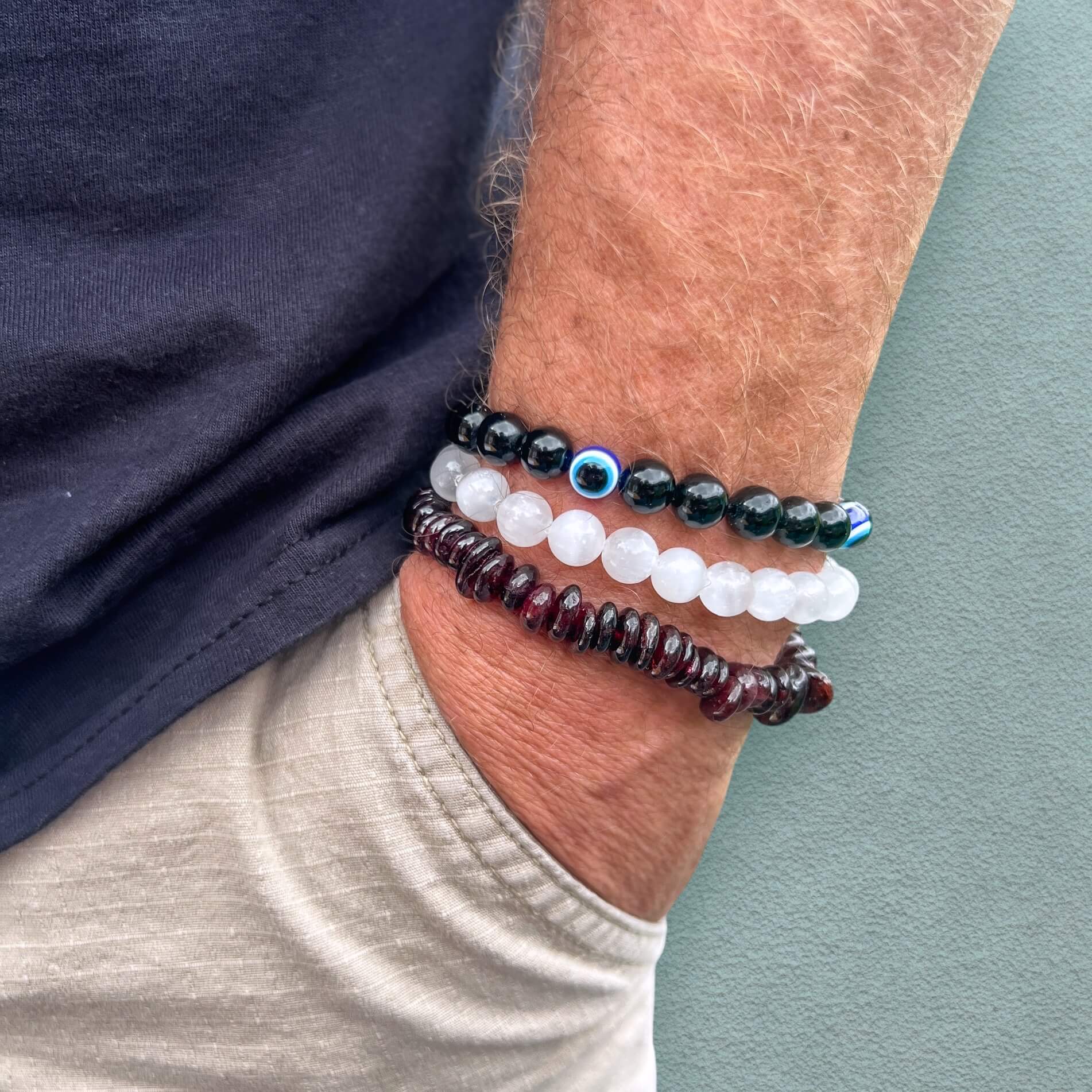 Close-up of a man's wrist wearing multiple crystal bead bracelets on a neutral background