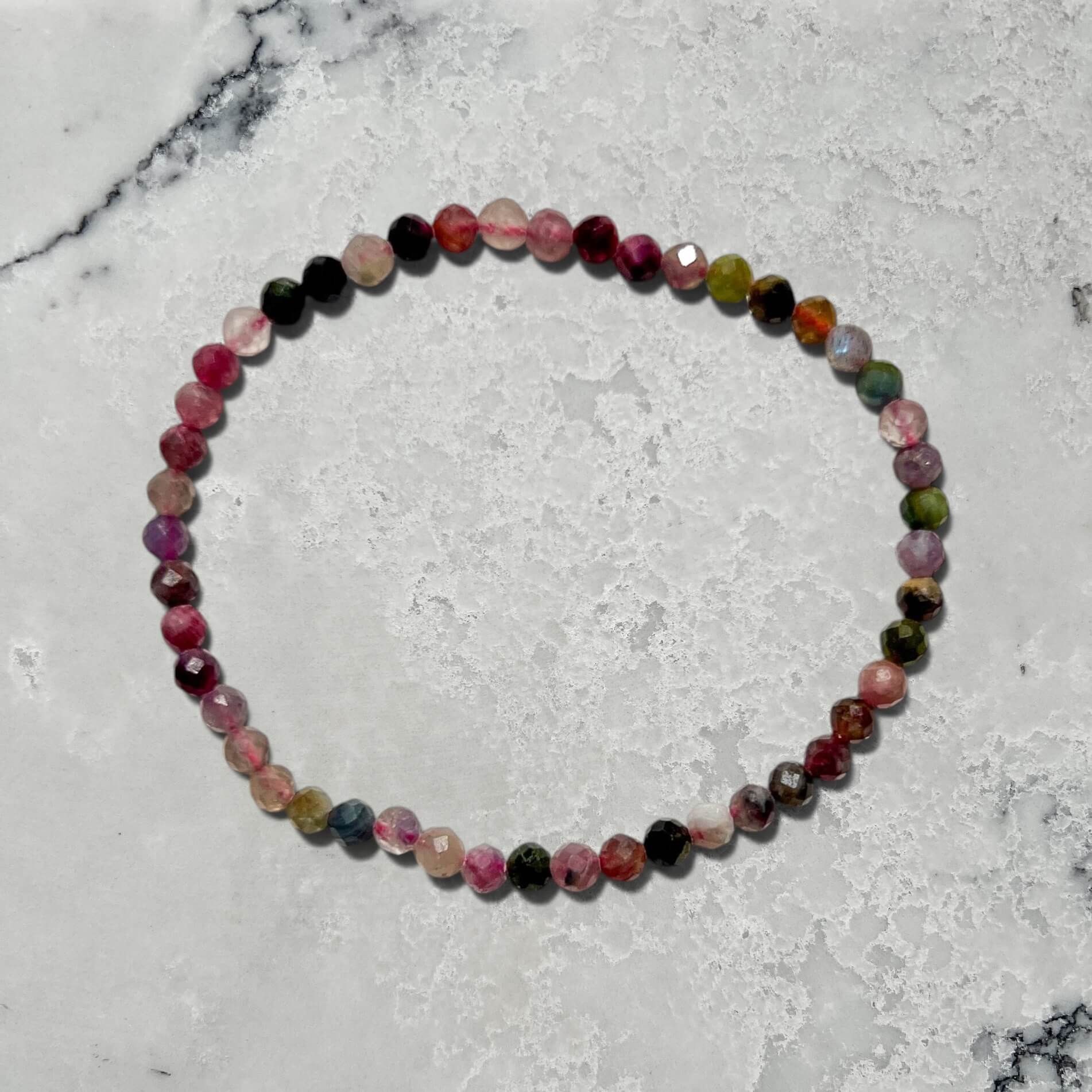 Multi-coloured shades of pink Mixed tourmaline faceted gemstone bead bracelet on a marble surface