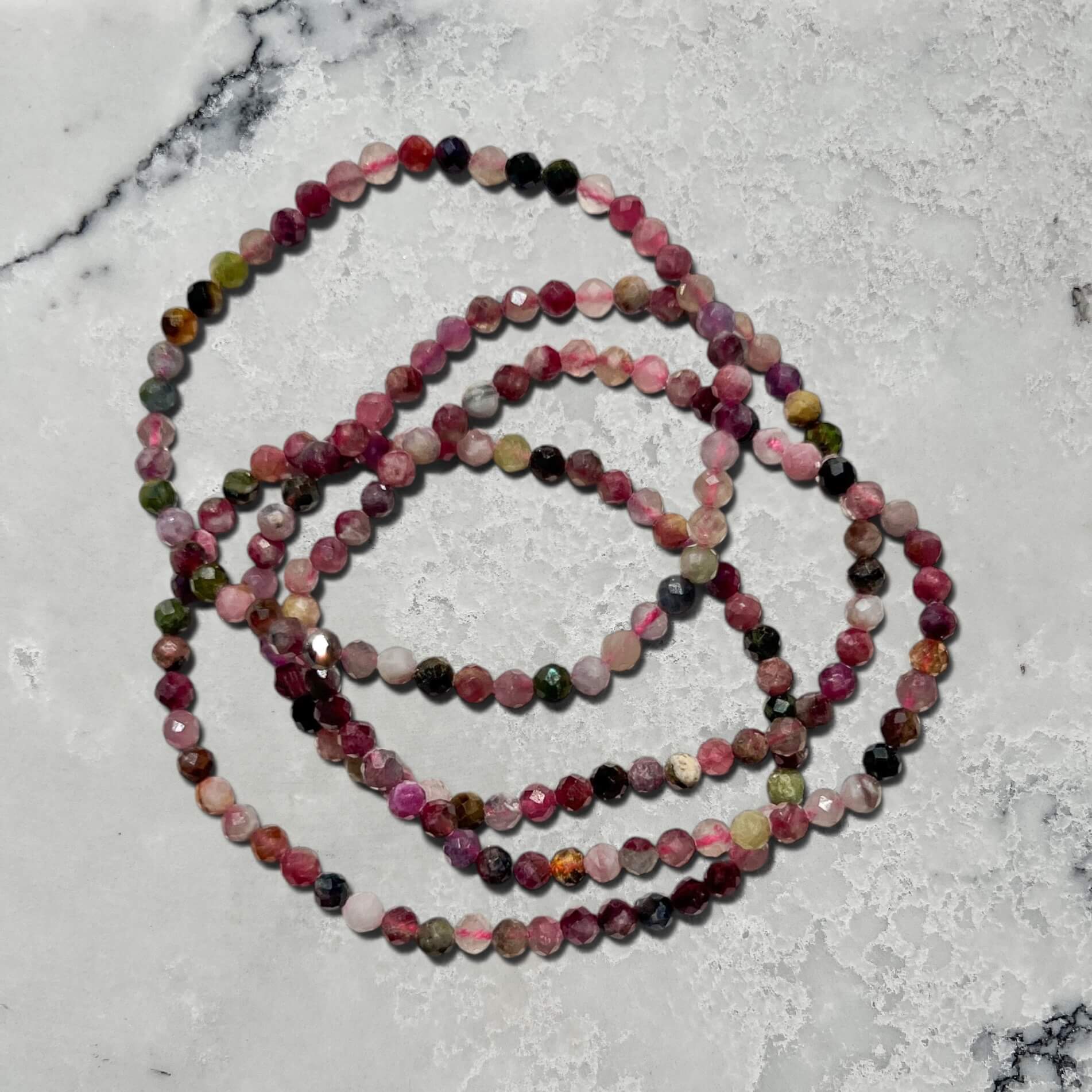 A stack of four Multi-coloured shades of pink Mixed tourmaline faceted gemstone bead bracelets on a marble surface