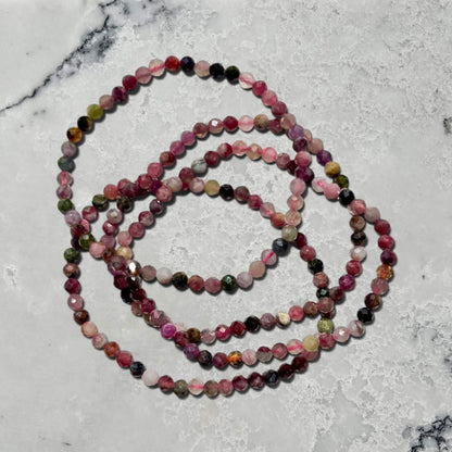 A stack of four Multi-coloured shades of pink Mixed tourmaline faceted gemstone bead bracelets on a marble surface