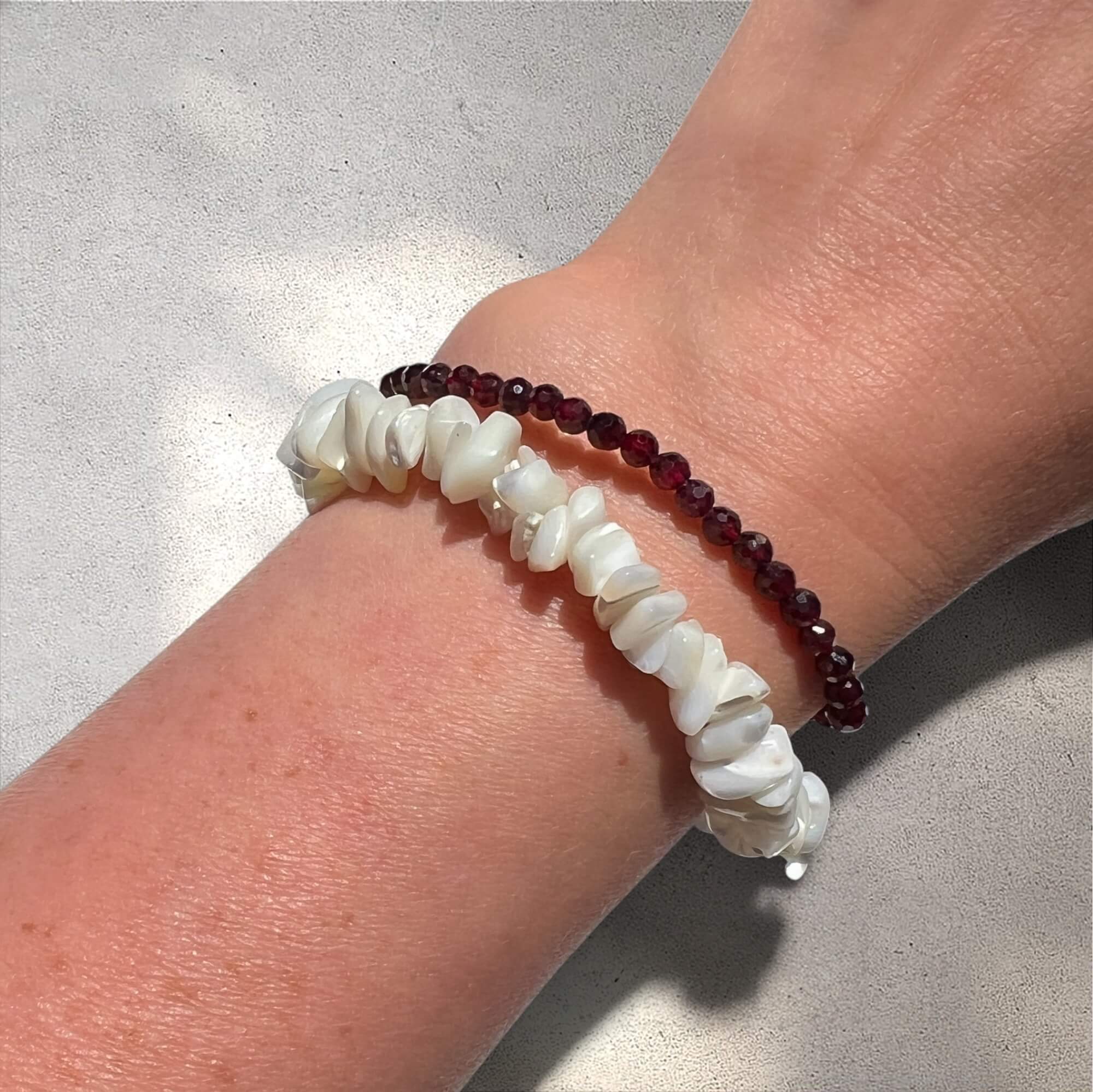 Stack of two bracelets with white mother of pearl and red garnet beads on a wrist against a neutral background
