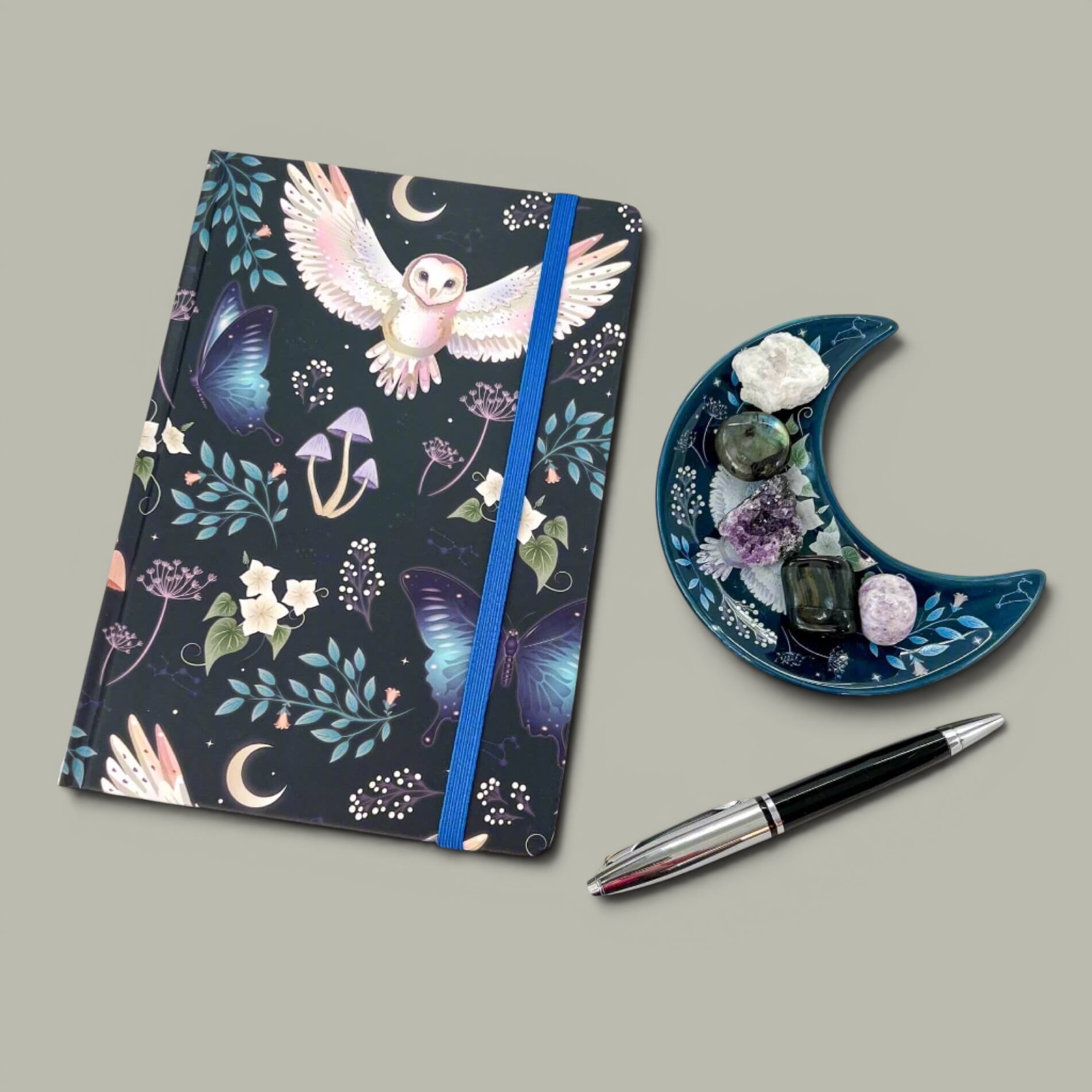 Rock + Realm Crystals dark blue journal with mystical owl, butterflies, mushrooms, and moon design. Blue elastic closure.