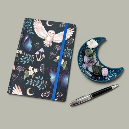 Rock + Realm Crystals dark blue journal with mystical owl, butterflies, mushrooms, and moon design. Blue elastic closure.