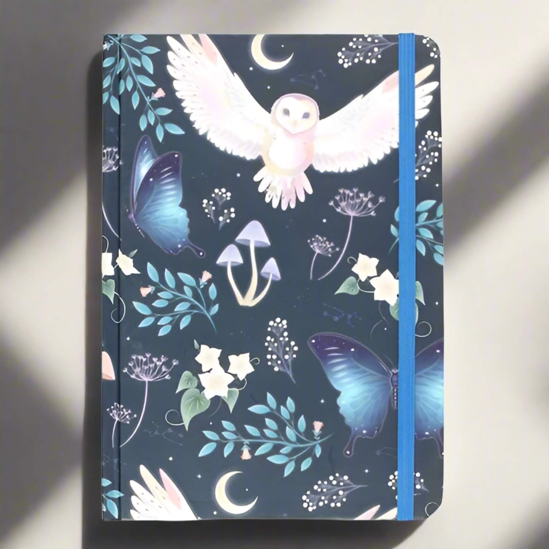 Rock + Realm Crystals blue mystical owl journal with butterflies, mushrooms, moon, and stars. Hardcover notebook with elastic closure.