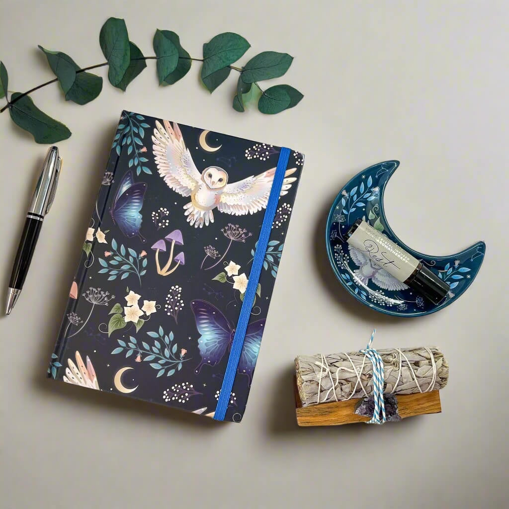 Rock + Realm Crystals dark blue journal with mystical owl, butterflies, moons, and mushrooms. Blue elastic closure.