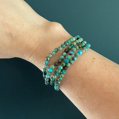 Natural Turquoise faceted crystal bead bracelets on a wrist against a eucalyptus green background