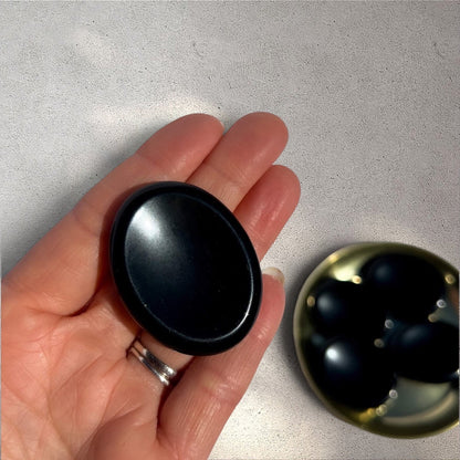 Rock + Realm Crystals black obsidian worry stone with thumb indentation held in hand.