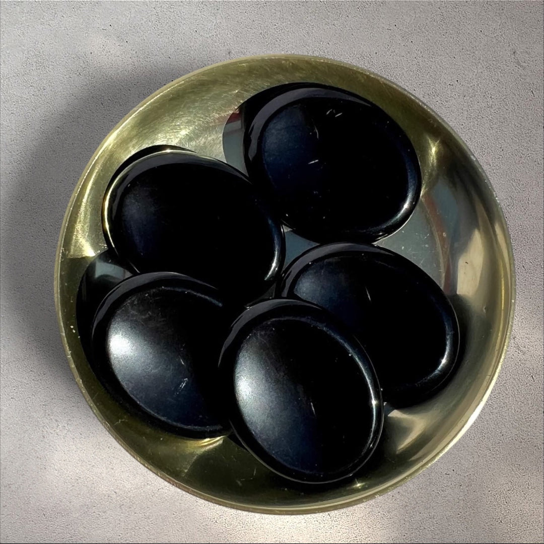 Rock + Realm Crystals polished black Obsidian worry stones with thumb indentation in a brass bowl from above