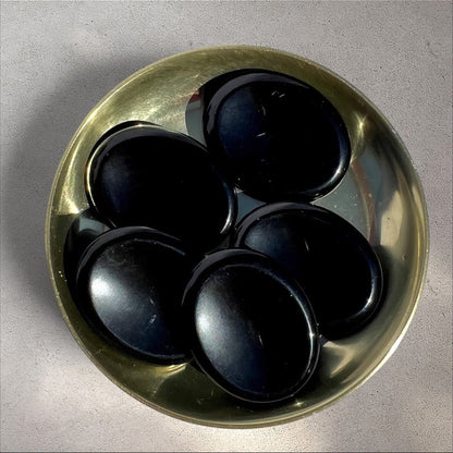 Rock + Realm Crystals polished black Obsidian worry stones with thumb indentation in a brass bowl from above