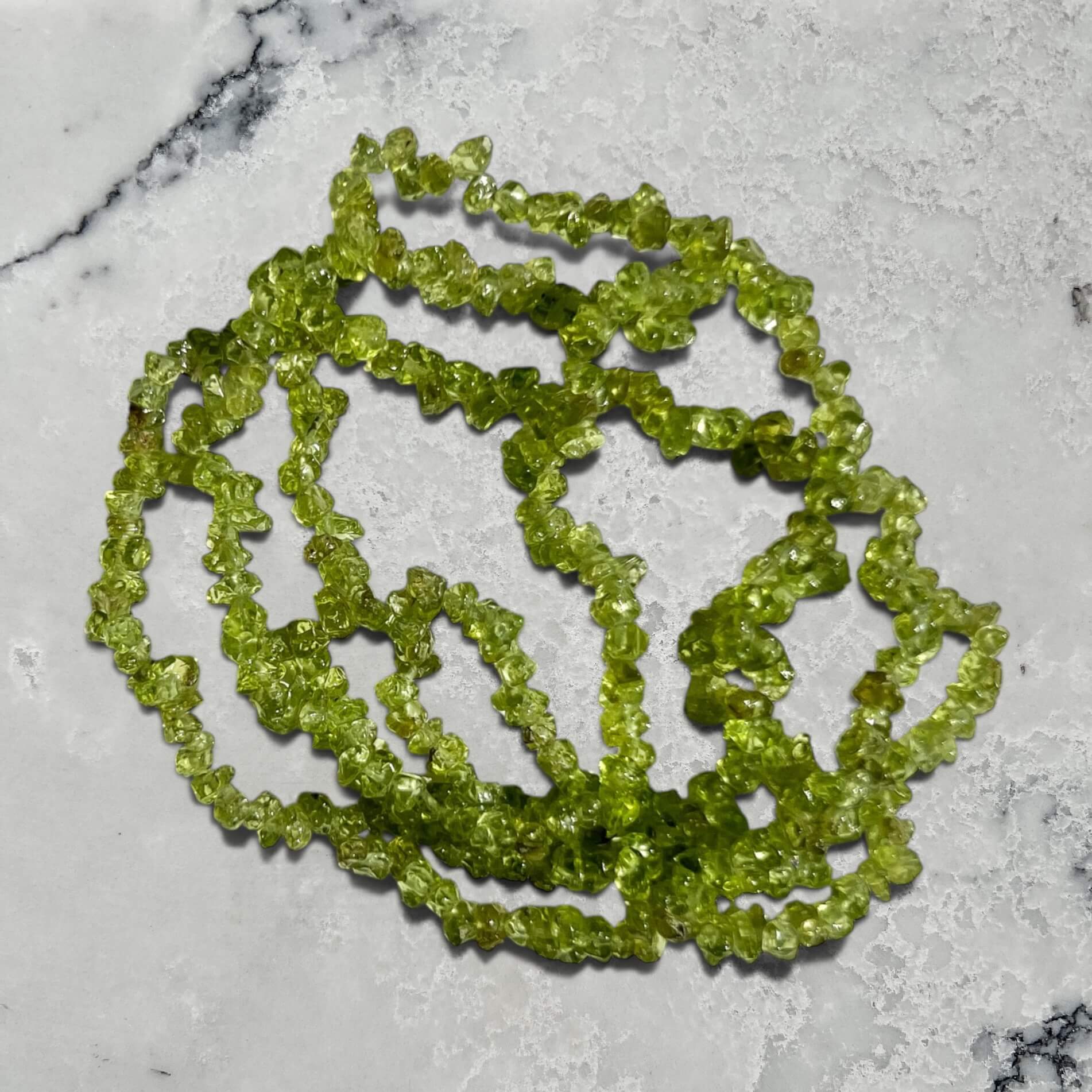 Stack of vivid green peridot gemstone chip bracelet on a grey marble surface