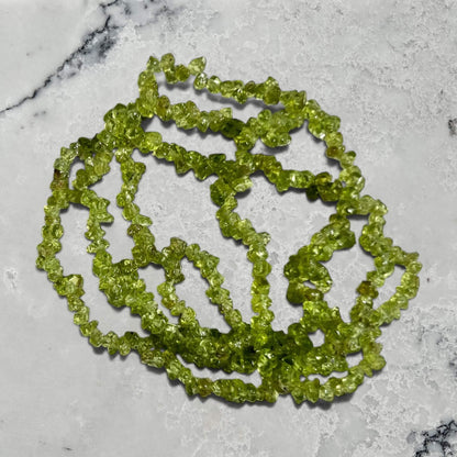 Stack of vivid green peridot gemstone chip bracelet on a grey marble surface