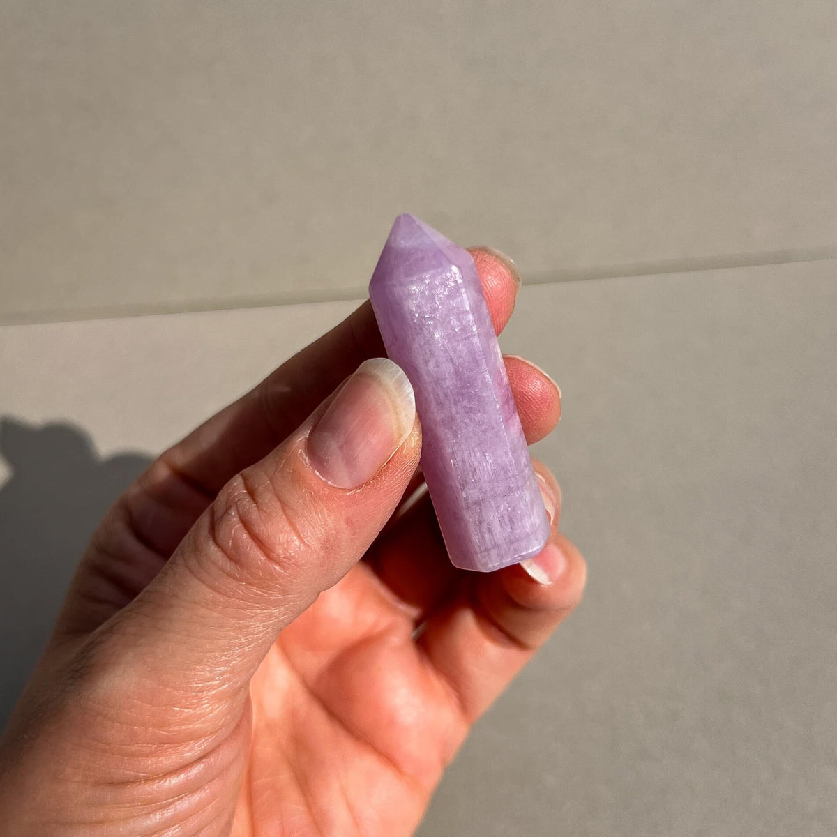 A hand holding a polished pink kunzite gemstone point against a neutral beige background