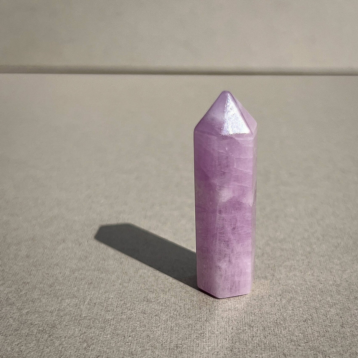 A polished lilac pink crystal point tower standing upright on a textured gray surface, casting a soft shadow to the left.