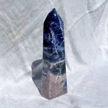 Blue and pink sodalite crystal obelisk tower on a white fabric background