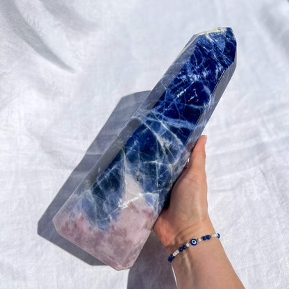 Hand holding a large blue and pink sodalite crystal tower against a white background