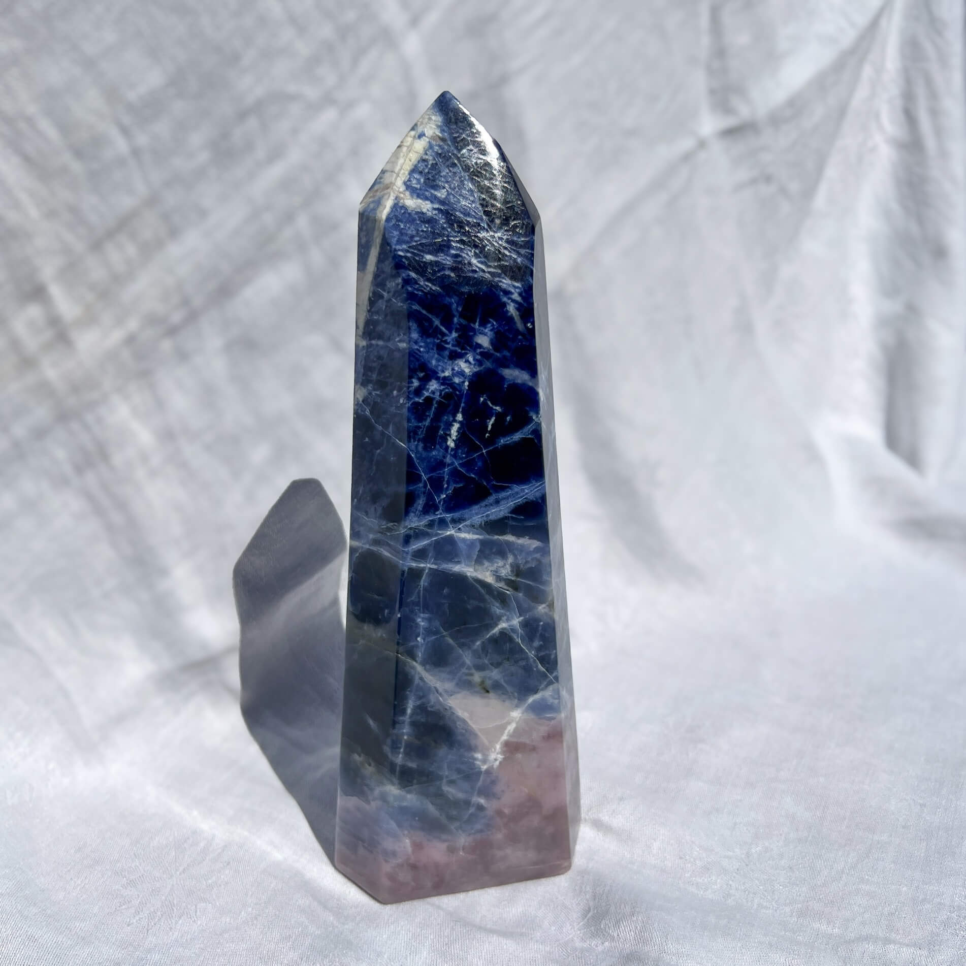 Large Sodalite Crystal tower with blue and pink patterns on a white fabric background