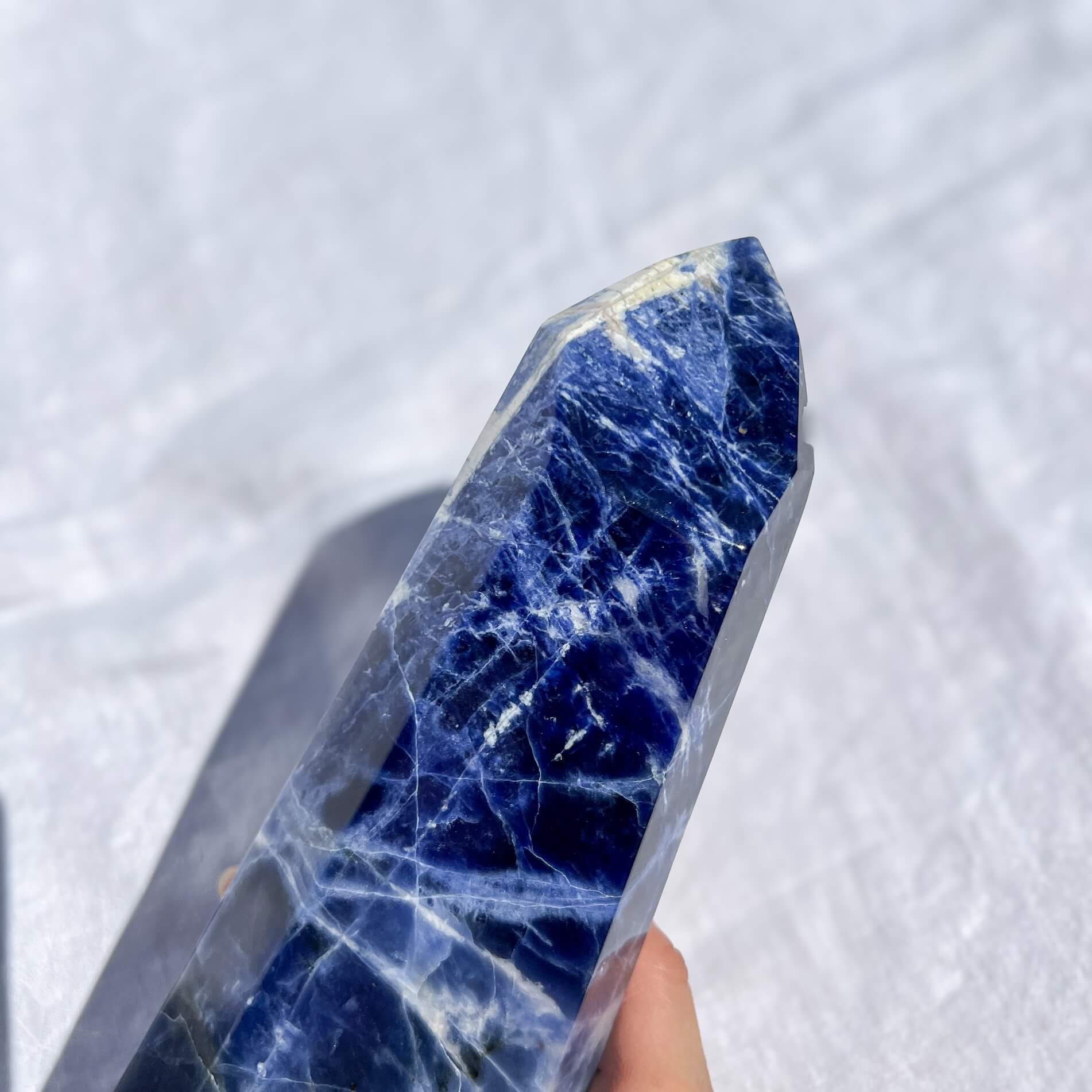 Blue and white sodalite crystal tower point held against a white background