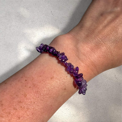 Purple amethyst crystal chip bracelet on a woman's wrist against a neutral background