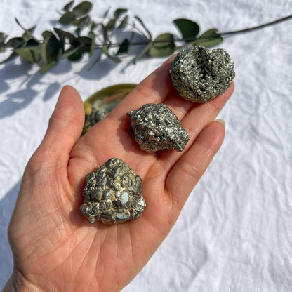 An outstretched hand holding three small golden pyrite crystal clusters shining in the sun's glow