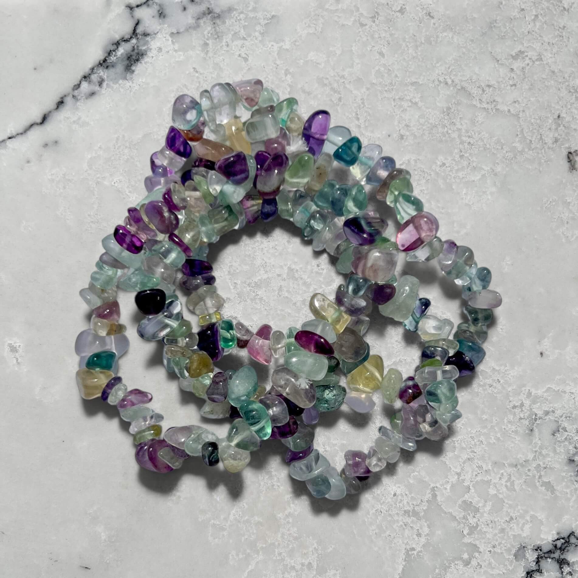 Stack of Multicolored rainbow fluorite gemstone chip bracelets on a marble surface