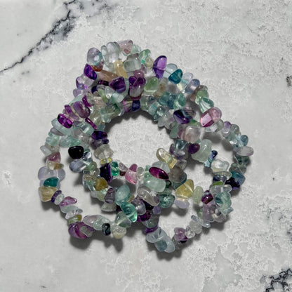 Stack of Multicolored rainbow fluorite gemstone chip bracelets on a marble surface