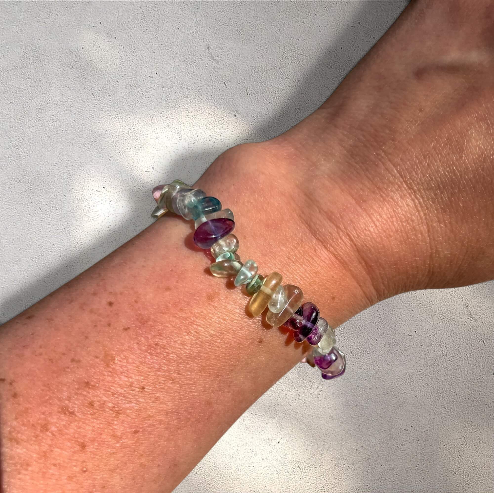 Multicolored rainbow fluorite gemstone chip bracelet on a woman's wrist against a neutral background
