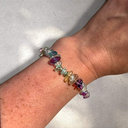 Multicolored rainbow fluorite gemstone chip bracelet on a woman's wrist against a neutral background