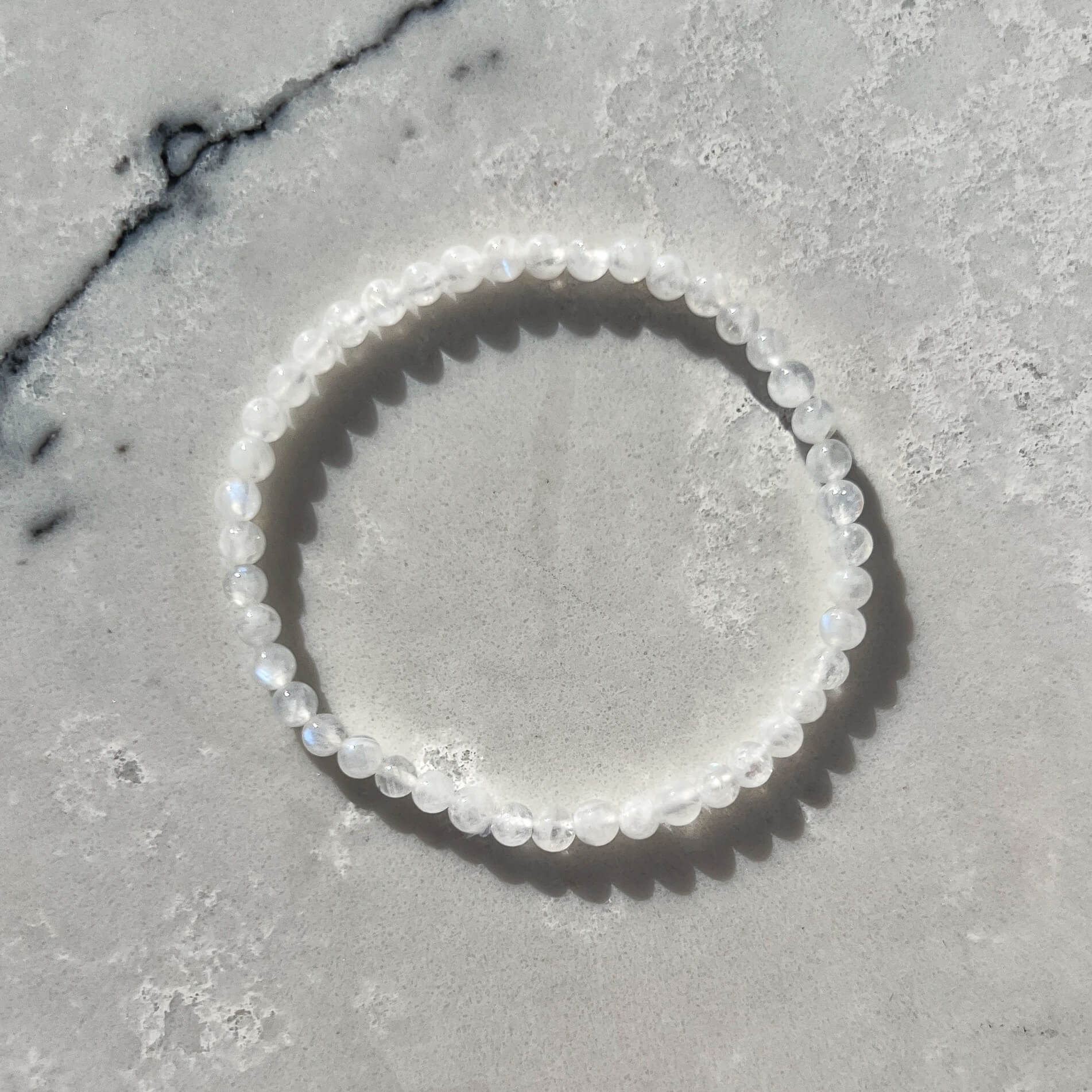 white moonstone crystal bead bracelet with subtle blue flashes on a white marble surface