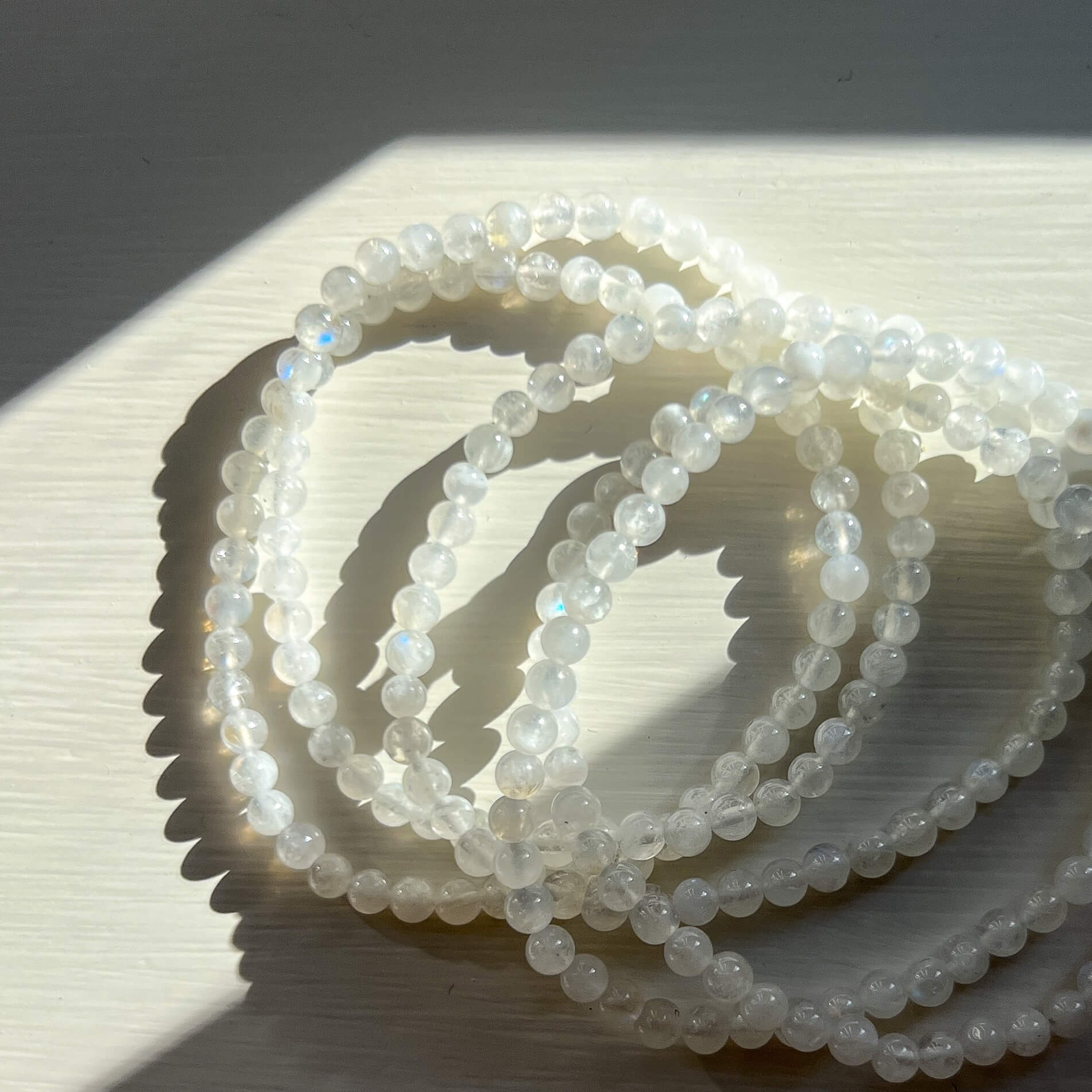 Stack of white moonstone crystal bead bracelets showing blue iridescent flashes in a sun dappled shot