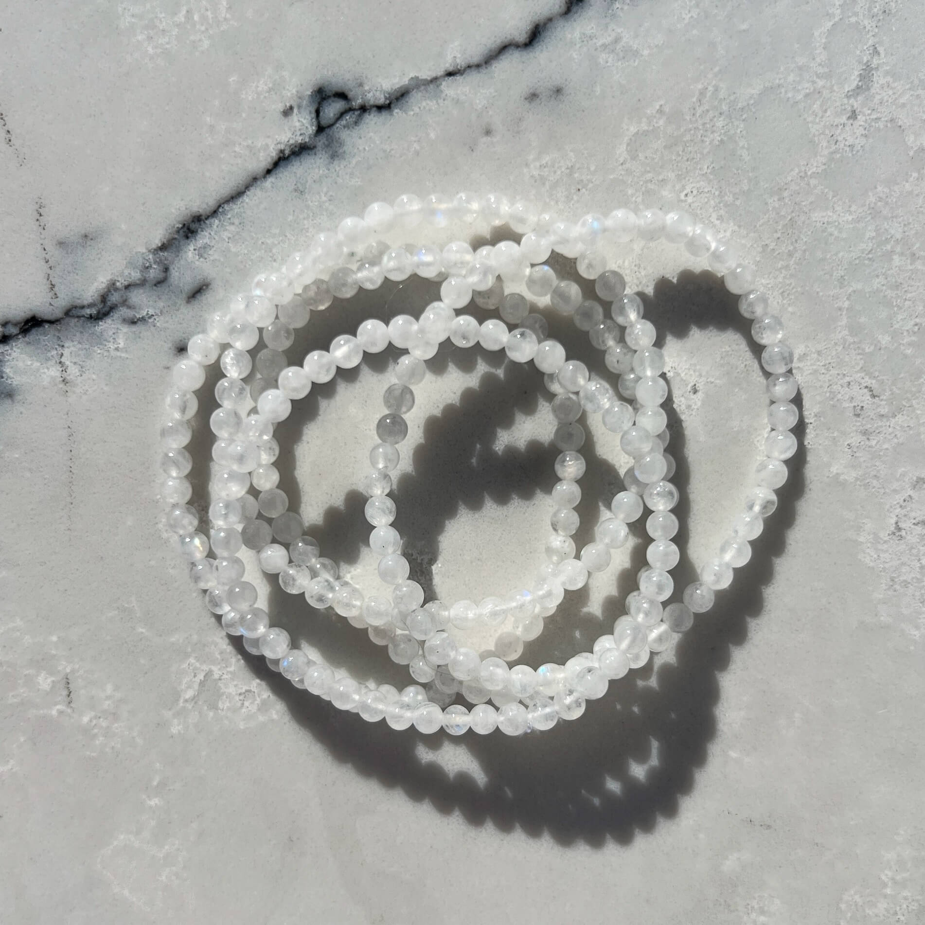 Set of four white moonstone crystal bead bracelets stacked on a white marble surface